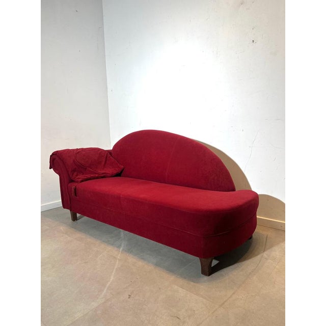 Elegant vintage chaise lounge upholstered in deep red velvet fabric. The asymmetrical design with one classic scroll arm...
