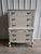 An elegant French Provincial tallboy dresser featuring graceful curves, ornate carved detailing, and a soft neutral finish...