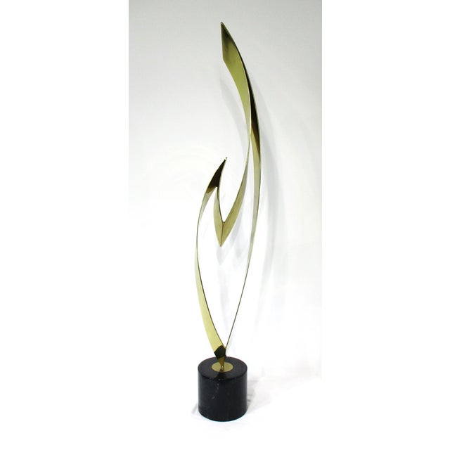 A stunning large sculpture in the form of a fire flame in brass mounted on a rounded black marble base with streaks of...