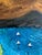 Original painting by L. Romo featuring a colorful lakeside village beneath warm brown mountains and a swirling, heavily...