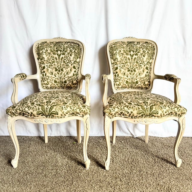 A charming pair of French Provincial–style armchairs featuring beautifully carved frames in a soft, antiqued cream finish....