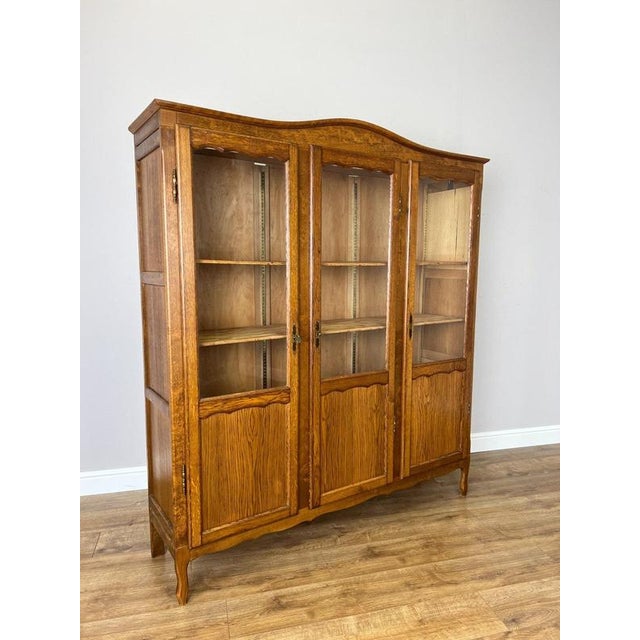 A charming Vintage French Louis bookcase in oak, featuring three glazed front sections, a shaped top profile and elegant...