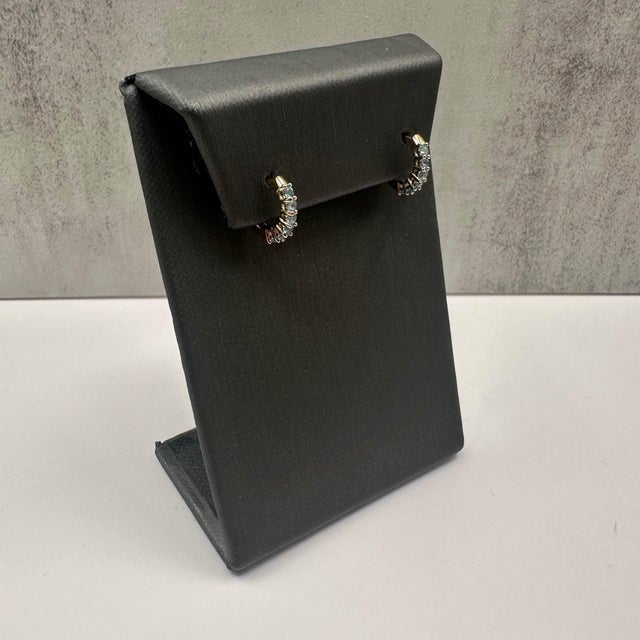 These stunning Blue Topaz Huggies in 10kt yellow gold feature 12 vibrant, approximately 2mm round blue topaz stones,...