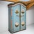 Light blue hand-painted fir-wood armoire with two doors, arched pediment, and a molded cornice. The chamfered corners and...
