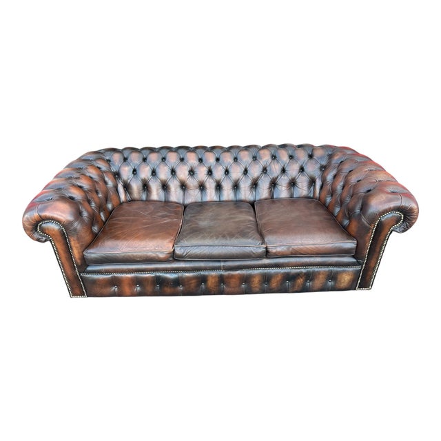 Classic English Chesterfield sofa upholstered in rich brown leather with deep button tufting, rolled arms, and brass...
