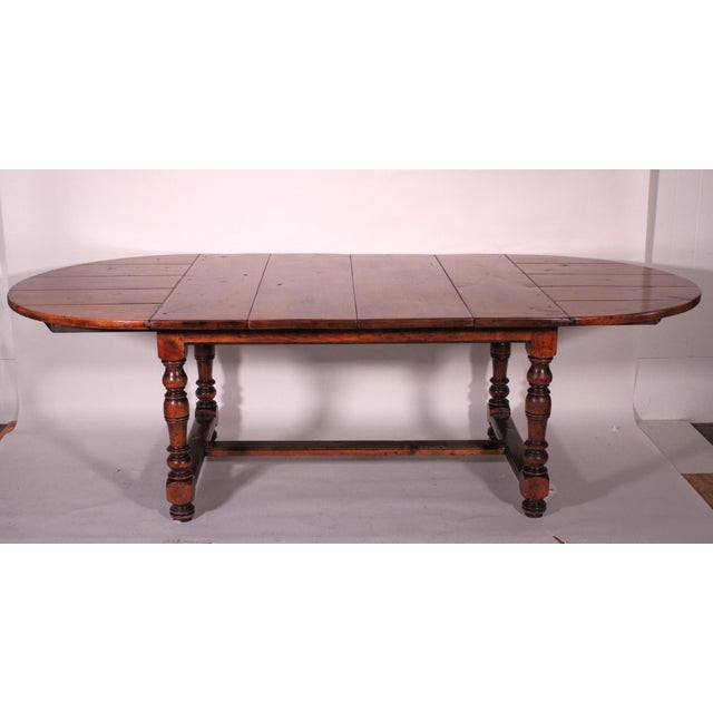 'Baroque style elm wood dining room table, circa 1980's. With an oval plank style top, baluster turned legs, joined by an...