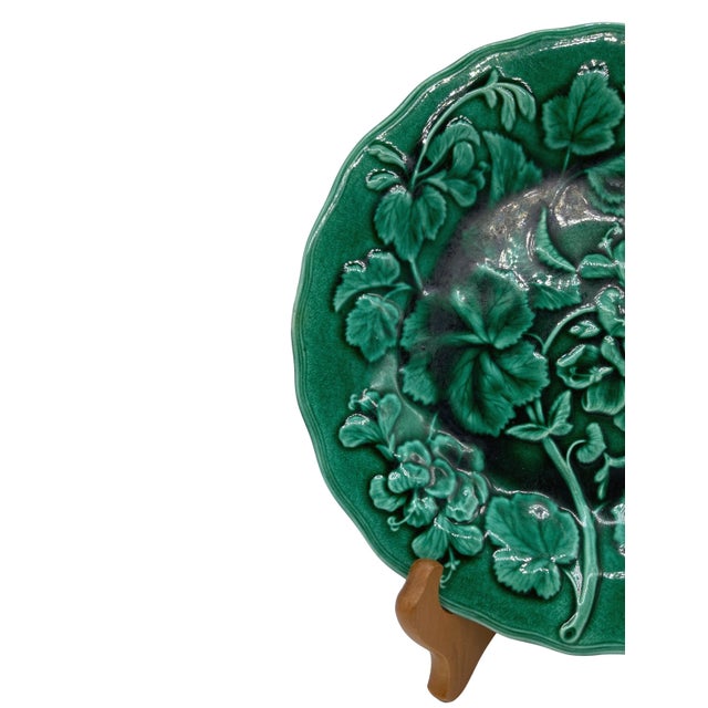English majolica green-glazed 9-inch plate, with relief molded geranium plants and blossoms and shaped rim, the reverse...
