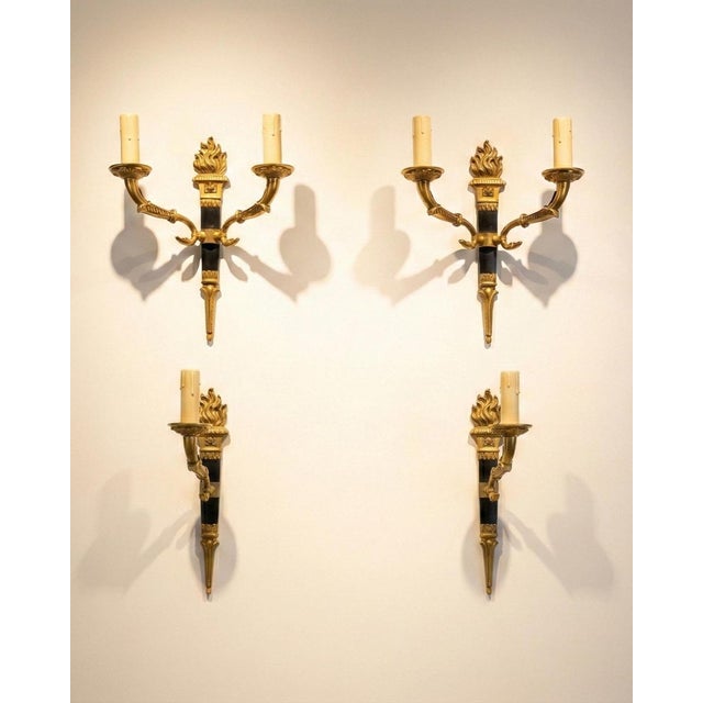 A magnificent set of four empire-style gilt bronze wall sconces, each centred on a bold torch motif with a black column...