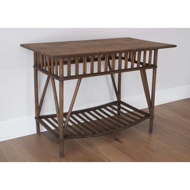 Charming mid century rattan table with a slatted apron and decorative bottom shelf with a downward bow. Rattan is...