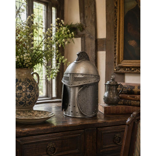 A vintage pewter ice bucket formed as a medieval knight’s helmet, detailed with riveted construction, a pierced visor, and...