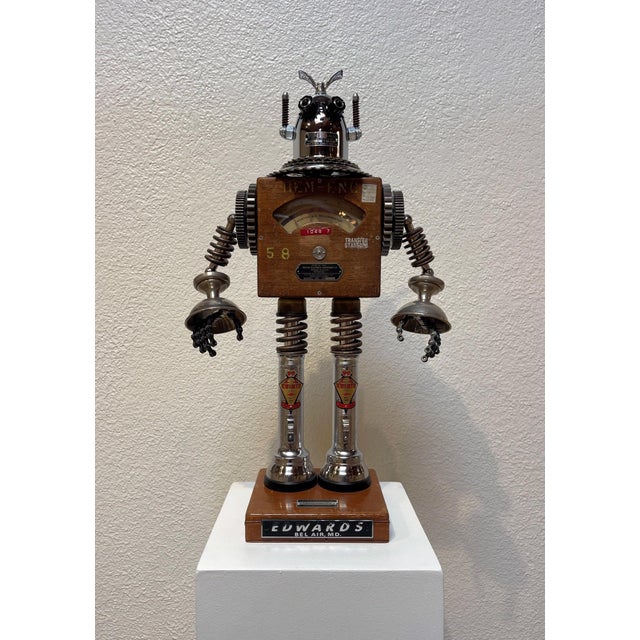 This found object assemblage features a whimsical robot figure, crafted from an eclectic mix of vintage materials,...