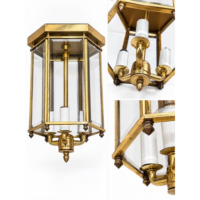 An elegant vintage ceiling lantern with a hexagonal brass frame and clear beveled glass. Three candle-style lights are set...