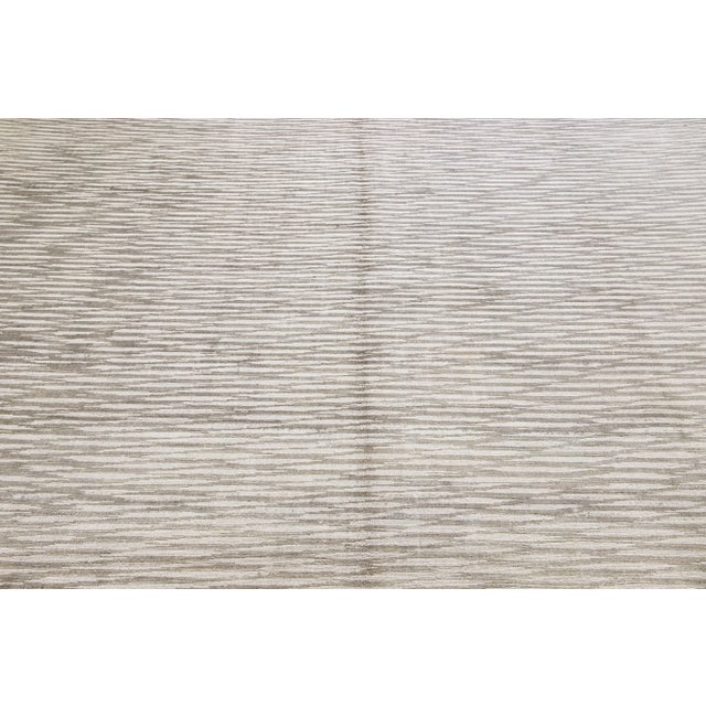 This exquisite contemporary wool and silk rug showcases a striking gray base adorned with a stunning geometric pattern...