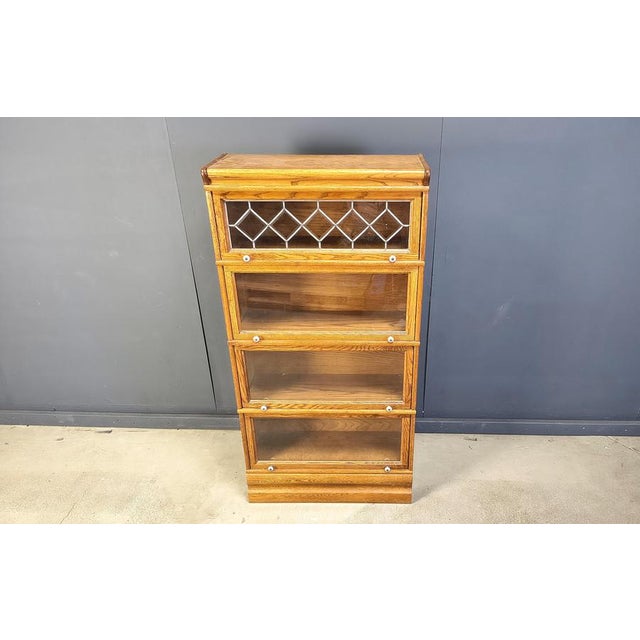 Crafted from oak with a timeless appeal, this barrister-style bookcase has four tiers with self-storing glass doors. The...