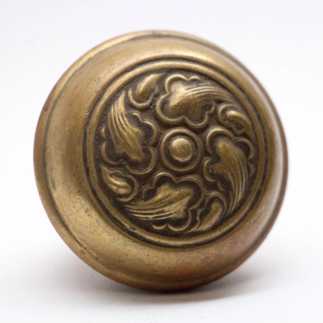 Brass door knob with a three fold swirl pattern. It is part of the E-14100 group in the 1905 catalog. The manufacturer is...