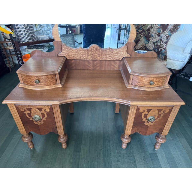 A Depression-era American vanity in walnut and burl walnut veneers, with drawer fronts and accents in quilted maple. The...