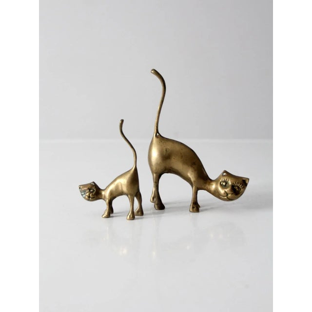 This is a pair of mid-century brass cat figurines. Stretching their backs, the cat and kitten figurines feature clean,...