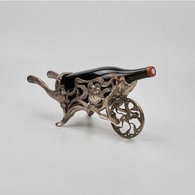 Wine bottle holder in the form of a gardener′s wheelbarrow, shaped and decorated with the theme of a sprouting flower. The...