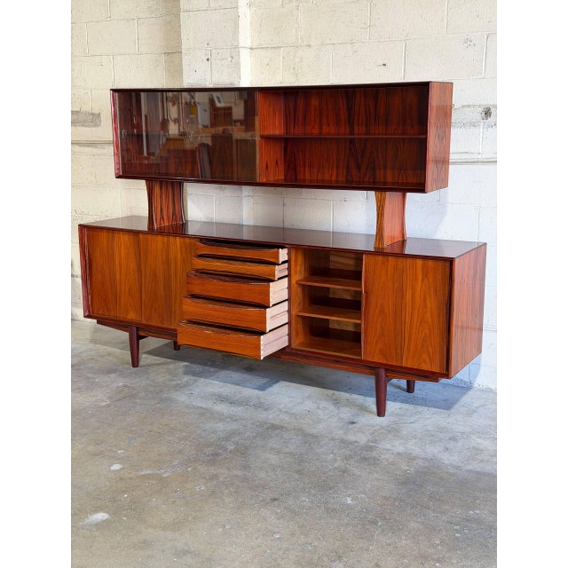 This two-piece sideboard and hutch features a striking architectural profile with an elevated glass display section. The...