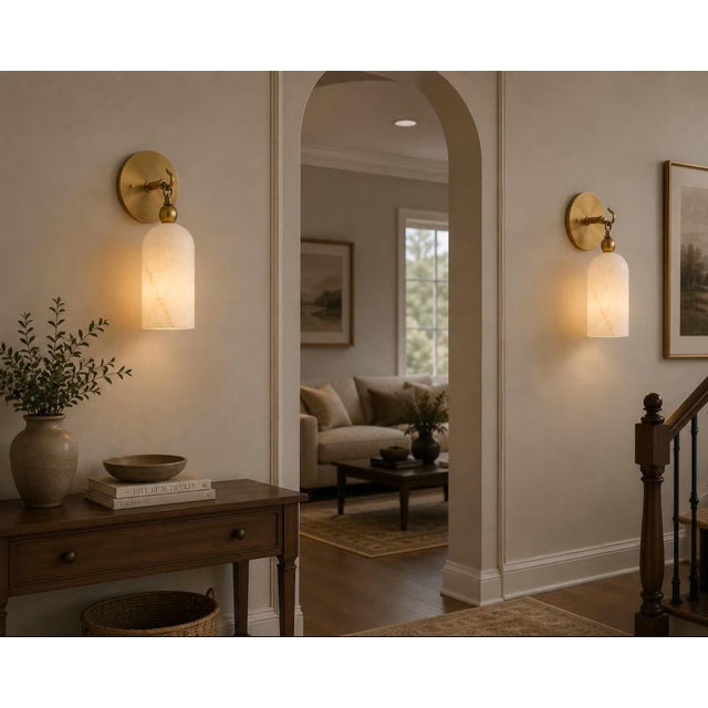 Add a warm architectural accent with this handcrafted brass wall sconce, featuring a natural alabaster cylinder shade...