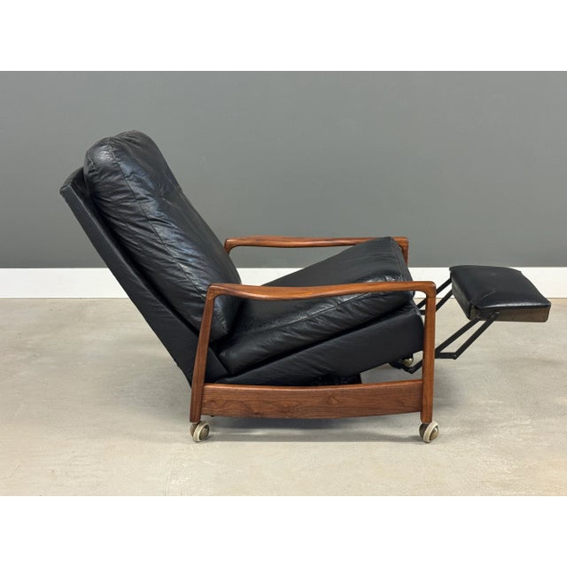 A mid century modern walnut reclining lounge chair with black vinyl upholstry with minor imperfections shown designed by...