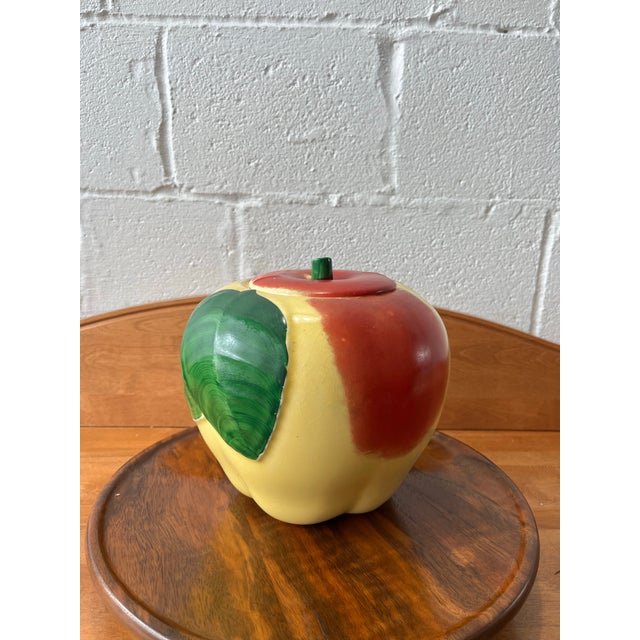 A charming mid-century ceramic apple-form cookie jar, featuring a softly rounded silhouette accented by a bold, sculptural...