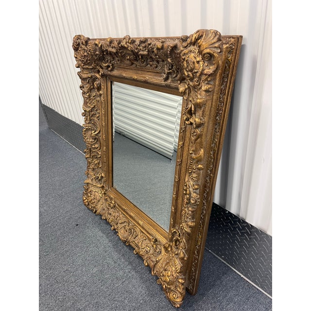Ornate late 20th century wall mirror by John-Richard featuring an elaborately carved giltwood frame with scrolling...