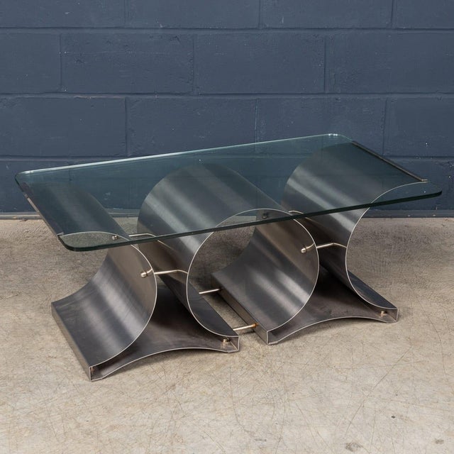 A sculptural brushed steel and glass coffee table designed by françois monnet for kappa in france during the 1970s. The...