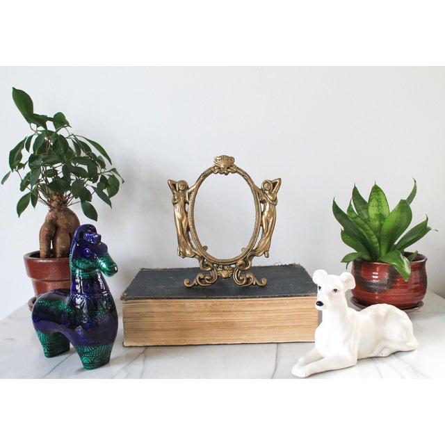 Antique Art Nouveau solid brass picture frame. This oval easel-back frame features two gowned female figures flanking an...