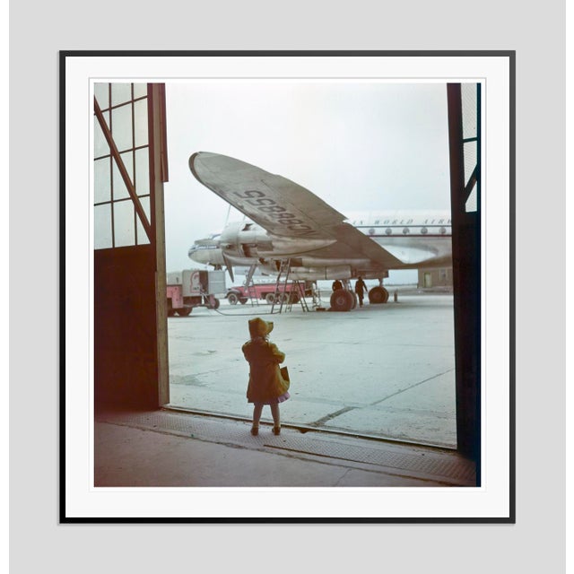 Young Traveller by Toni Frissell A young girl stands in her raincoat awaiting a plane to be refilled for her travels....