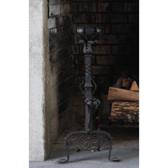 A pair of ornate and massive Gothic Revival style wrought iron andirons with torch finials, acanthus leaf detailing, rope-...