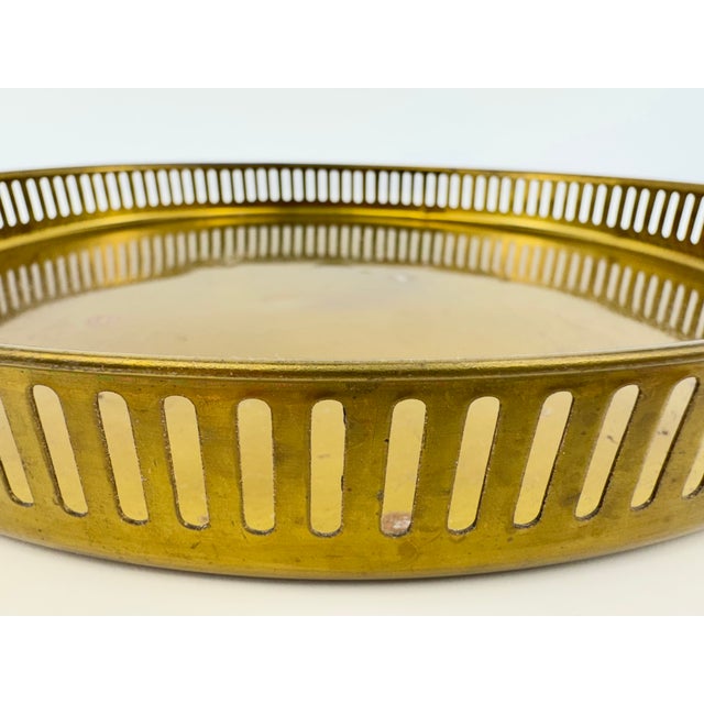 A vintage round brass-tone gallery tray featuring a continuous pierced metal railing with slender vertical openings and a...