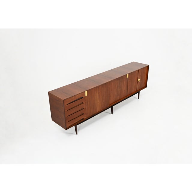 A wooden sideboard comprising five drawers, two lockable doors concealing a shelf, and two sliding doors each concealing a...