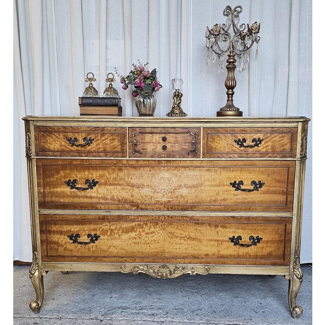 This antique French provincial style dresser features striking book matched burl wood grain and ornate gold leaf trim. The...