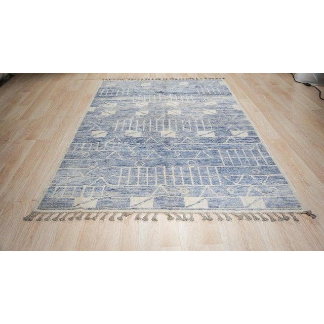 This blue wool rug features a hand knotted pile construction in the style of a traditional Berber carpet. Crafted in...