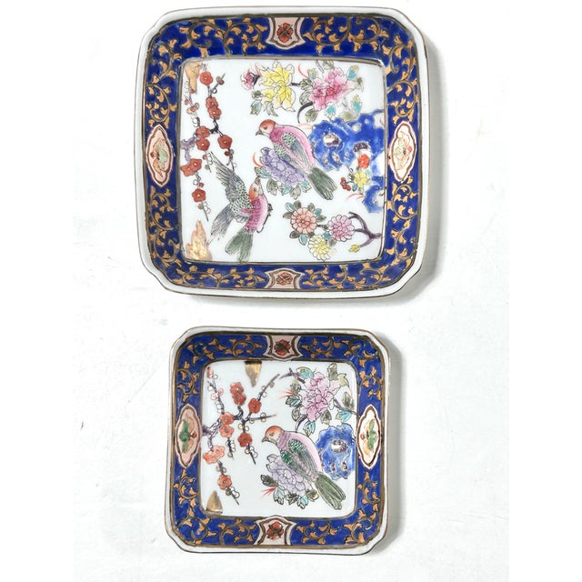 A pair of chinoiserie-style porcelain catchall trays with rich cobalt blue borders, gilt scrollwork, and colorful bird-...