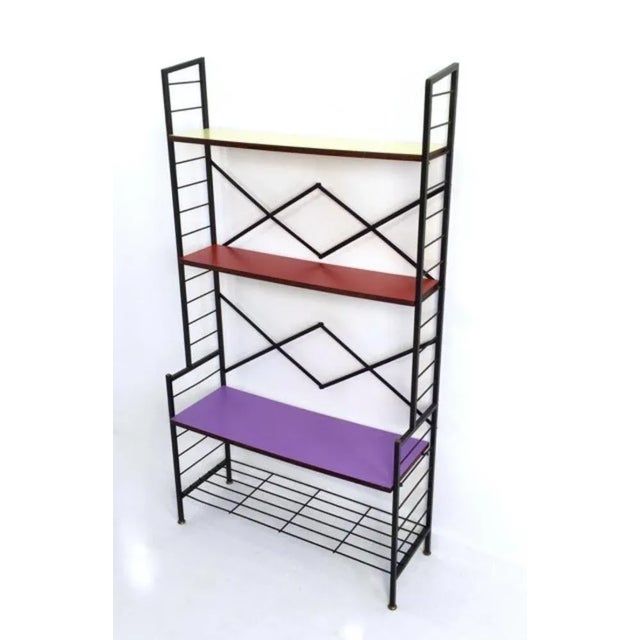 Made in Italy, 1960s. This shelving unit is made from varnished iron with brass feet caps and wooden shelves that are...