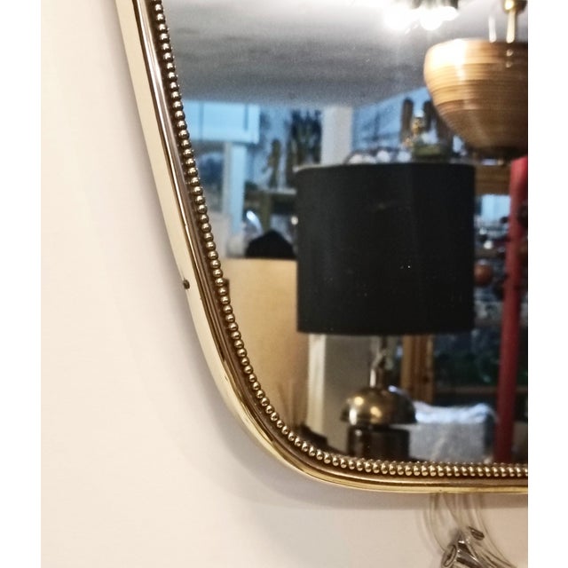 An Italian wall mirror in brass, dating from around the 1950s. The mirror has slightly tapered sides and a gently wavy...