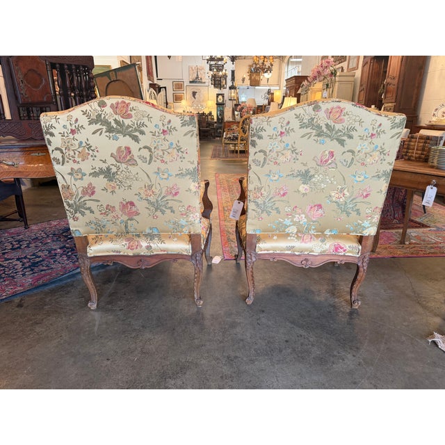 This elegant pair of antique French Louis XV style bergère armchairs features hand-carved solid walnut frames with classic...