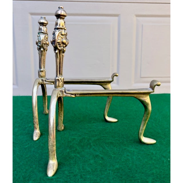 Antique pair of brass fire dogs (andirons). Ornate design, stylized floral/acanthus finials, and distinctively shaped...
