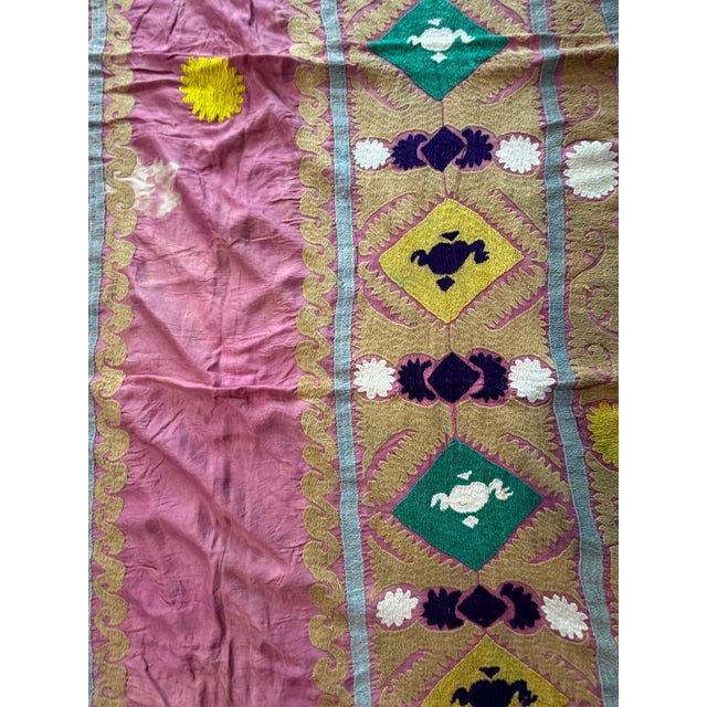 Hand-embroidered Suzani panel from Uzbekistan — a rose pink prayer niche framed by gold and teal diamond panels with...