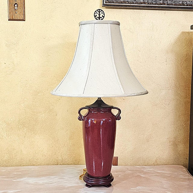 This refined vintage table lamp showcases a burgundy glazed ceramic urn-form body accented with sculptural side handles,...