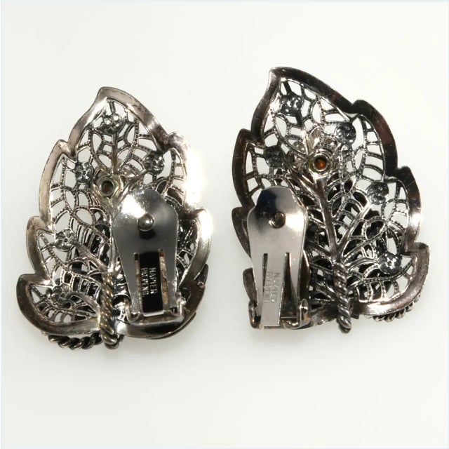 Vintage clip earrings crafted of silver plated filigree metal in a leaf design. They are also embellished with clear...