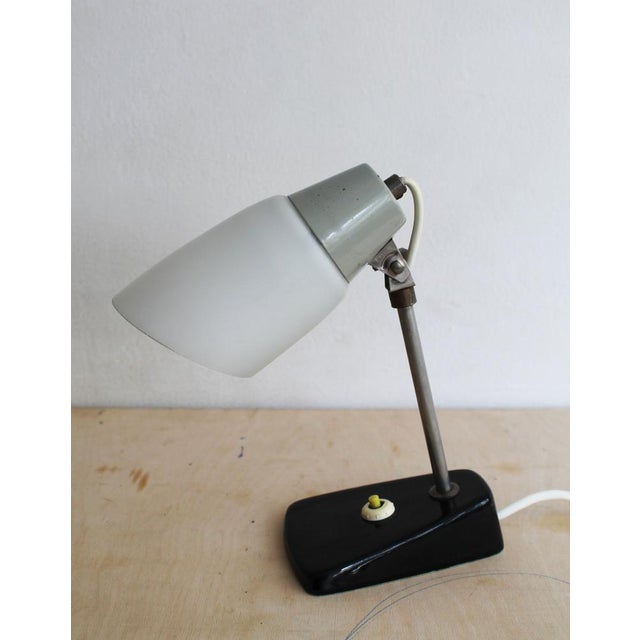 The lamp features an elegant black ceramic base manufactured by Ditmar Urbach, a slender steel stem, and an original milk-...