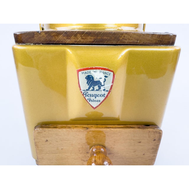 A charming mid-century French manual coffee grinder by Peugeot Frères, featuring a distinctive mustard-gold painted metal...