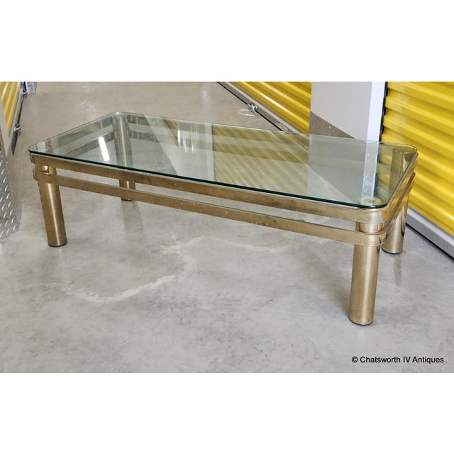 Vintage modern glass top living room coffee table. Tubular legs with flat bar supports with a rounded corner glass top. No...