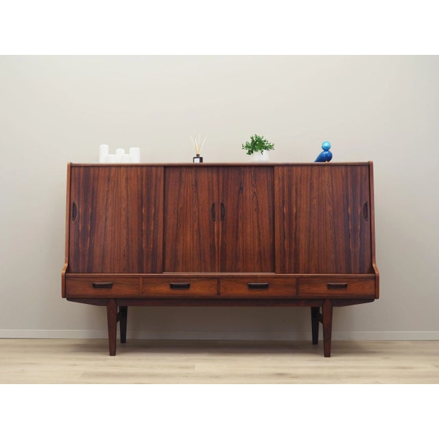 The highboard was made in the 1960s, Danish production. The structure is covered with rosewood veneer. The legs are made...