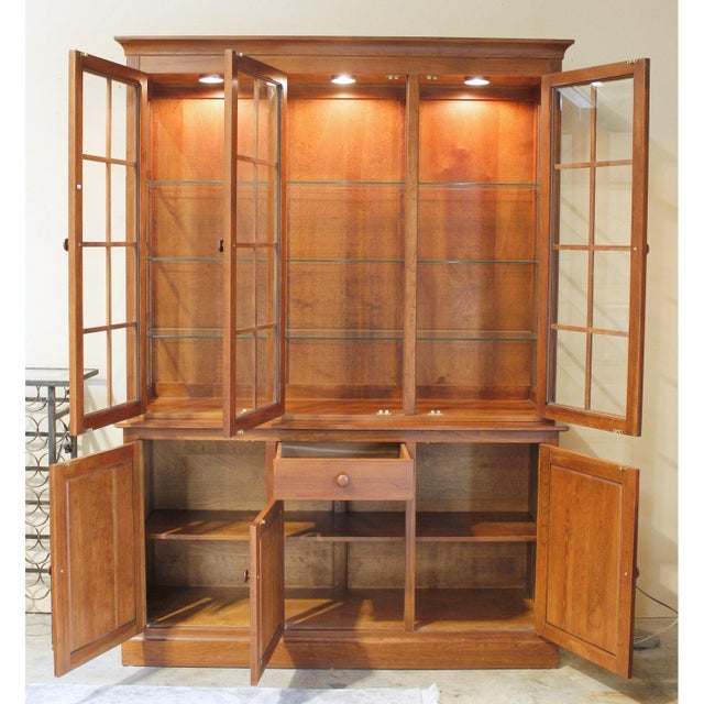 This solid cherry cabinet features a warm, rich finish with a three‑door glass hutch above, illuminated to showcase...