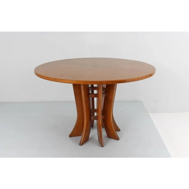 Beautiful round wooden dining table with an elegant central pedestal made up of shaped and rounded slats, positioned in a...