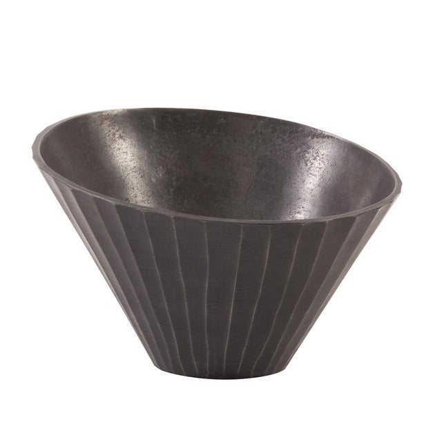 This metal bowl features an asymmetrical shape. It is characterized by a chiseled texture etched into the metal on the...